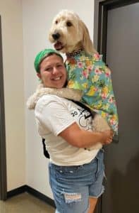 NCW employee holding their dog that is sporting a floral shirt.